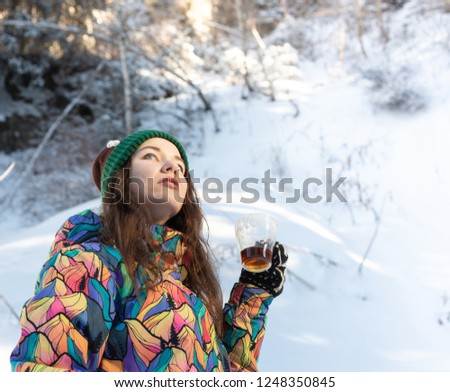 Girl enjoys the snow falls. Young woman in a knitted shape is drinking tea in the forest during a snowfall. Toned photo