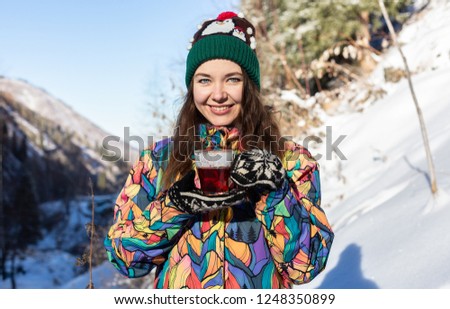 Girl enjoys the snow falls. Young woman in a knitted shape is drinking tea in the forest during a snowfall. Toned photo