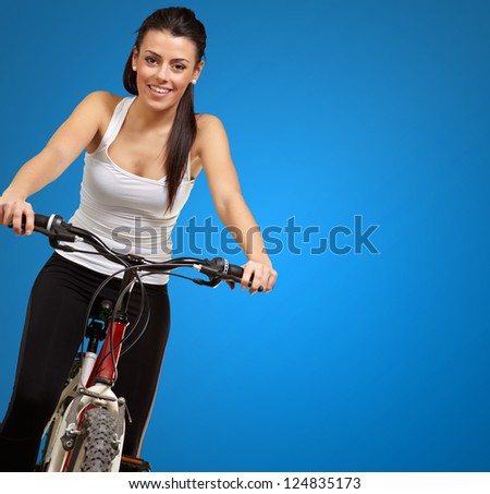 Portrait of a young girl sitting in bicycle isolated on blue background