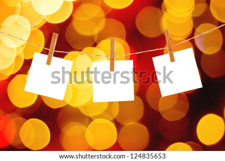 Blank paper cards hanging on clothespins against Christmas lights background