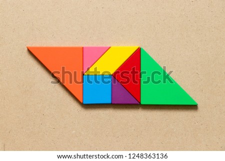 Color tangram puzzle in parallelogram shape on wood background