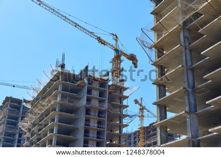 Apartment building under construction and cranes against the blue sky.