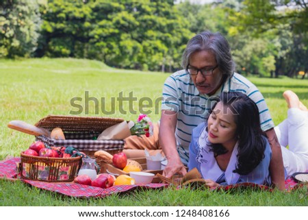 The old couple relax in park. In the morning Man hugging woman beside picnic basket.They are read a book in love and sweet.Life style, Exercise ,Photo concept  love and healthy.