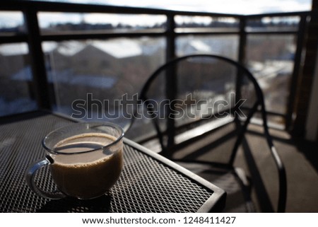 Coffee cup in sunlight with empty chair on balcony