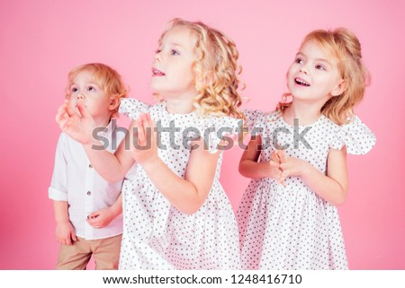 three adorable baby amazed and happy smiling birthday party.two little blonde girls twin sisters in a cute white dress and boy brother in the studio on a pink background,new year Christmas gift