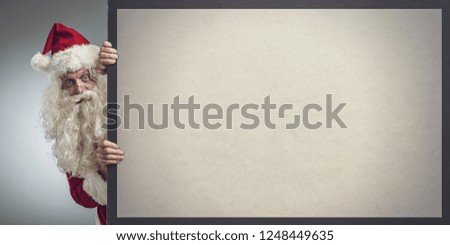 Funny Santa Claus peeking from behind Christmas advertisement blank sign with copy space, he is looking at camera