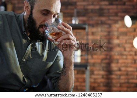 Handsome man holding glass of whiskey indoors. Space for text