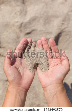 Hands of a young woman playing with sand. The sand pours through the hands of the girl.