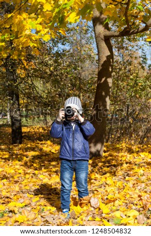 little boy with a camera photographs looking directly into the camera, a portrait in autumn park close-up.