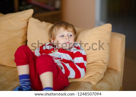 Happy adorable kid boy watching television while lying. Funny healthy child enjoying cartoons. Addiction concept. Toddler looking shows and film on tv at home.