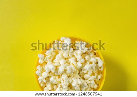Movie theater popcorn in a bowl on yellow background with copy space, top view