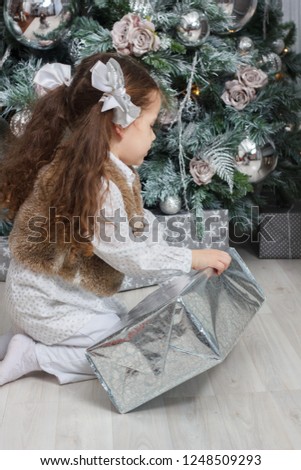 Little kid girl sitting at the floor near christmas tree with christmas gift at hands.