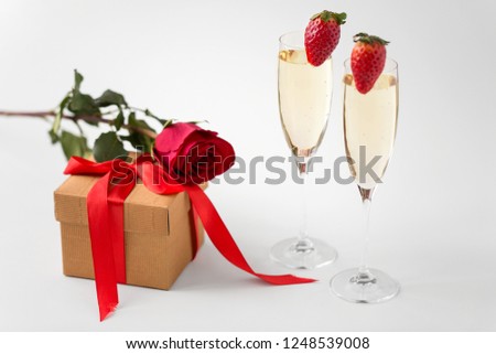 valentines day and holidays concept - two champagne glasses with strawberries and gift box with red rose on white background