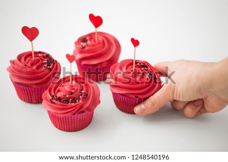 valentines day, food, baking and pastry concept - close up of hand taking cupcakes or muffins with red buttercream frosting and heart cocktail sticks