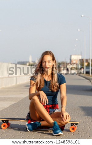 Teen girl with a longboard is sitting on a concrete surface