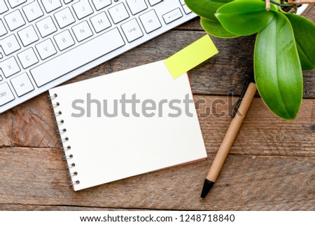 A blank notebook on the wood in the presence of a keyboard and a flower. View from above. High resolution photography.