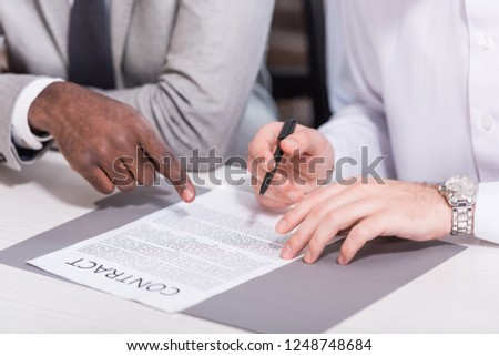 Cropped view of multicultural businessmen signing contract at office desk 