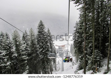 skiers and snowboarders climb up the slope on a six-seater chair lift in the snow-covered forest.