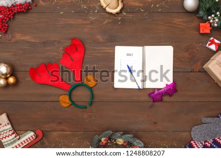 Notebook with goals for new year fancy eyeglasses and deer antlers headband isolated on wooden table top view close-up