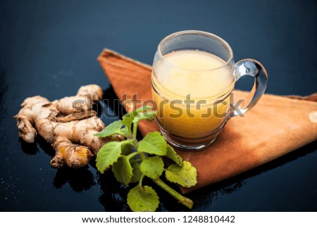 Close up of organic juice of ginger in a transparent glass on wooden surface with some raw ginger and ajwain leaves with it.