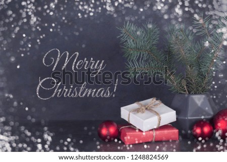 Merry Christmas card with silver text, fir branches in polygonal vase, gifts, red balls, snowflakes on gray background. Greeting card concept, top view, layout design