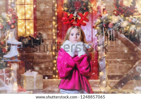 Pretty child girl is standing near the house decorated for Christmas with reindeer antlers on the head. Merry Christmas and Happy New Year.