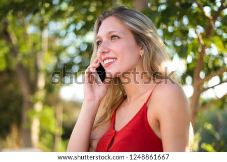 Young blonde girl keeping a conversation with the mobile phone with someone at outdoor