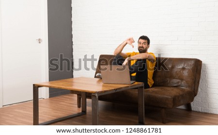 Man with his laptop in a room showing thumb down sign with negative expression