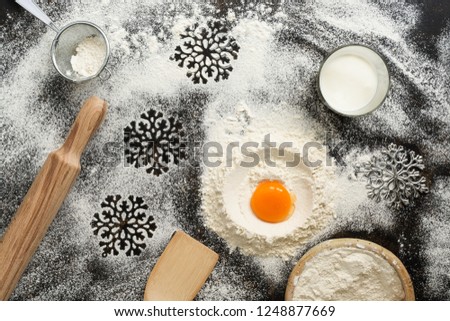 Christmas dark background with baking ingredients. Flour, egg, milk, rolling pin, sieve, snowflakes, spatula. Top view, place for text