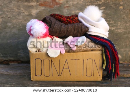     Donation box with warm winter clothes on old wooden background. 