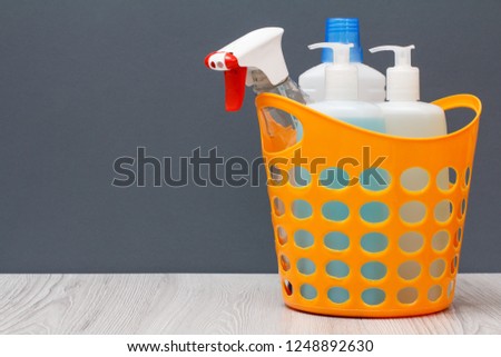 Plastic basket with bottles of dishwashing liquid, glass and tile cleaner, detergent for microwave ovens and stoves on gray background with copy space. Washing and cleaning concept.