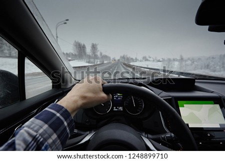 Driving a car in the winter in dangerous road conditions. View through the windshield of the car during the day. The hands of the driver on the steering wheel and the speedometer control.