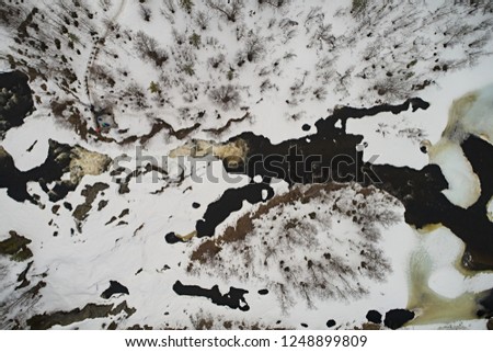 Aerial view of the taiga forest and frozen waterfall with a river in cloudy weather. Abstract winter landscape of northern country with drone.
