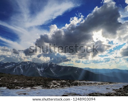 Rays of the setting sun through the clouds above the tops of snowy mountains. 