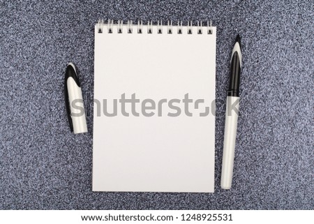 White spiral notebook with clean sheets with black and white pen on black glittery lighted background, top view.