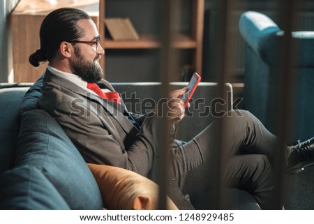Suit and tie. Bearded businessman wearing grey suit and red tie holding his phone reading message
