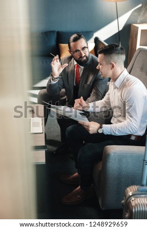 Giving instructions. Bearded prosperous boss wearing glasses giving some instructions his employee