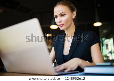 Serious woman employer checking e-mail on modern laptop computer while sitting in restaurant during work break in company. Proud female having webinar via  notebook device while resting in coffee shop