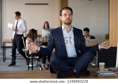 Business People working in coworking space, focus on millennial peaceful employee in formal suit sitting without shoes in lotus position on office desk practising meditation and visualization exercise Royalty-Free Stock Photo #1248983278