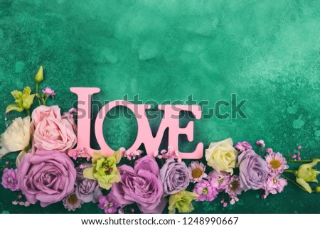 Valentines day concept with flowers and word "love" on green vintage background. Festive floral concept with clean space for text. Top view.
