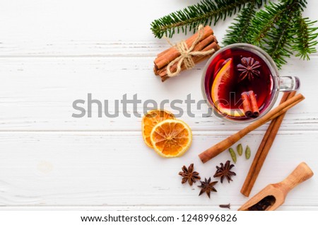 Hot red mulled wine in glass with orange, cinnamon sticks and star anise with ingredients on white wooden background. Spicy warm beverage. Seasonal Christmas mulled drink. Copy space. Top view.