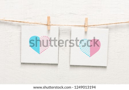 Valentine's Day. White pieces of paper with painted hearts pinned to rope with clothespin on light background