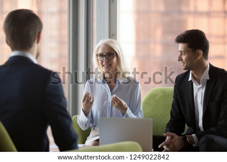 Business people sitting on comfortable couch in contemporary office near panoramic window. Middle aged company ceo and middle eastern ethnicity colleague talking with client discussing working details Royalty-Free Stock Photo #1249022842