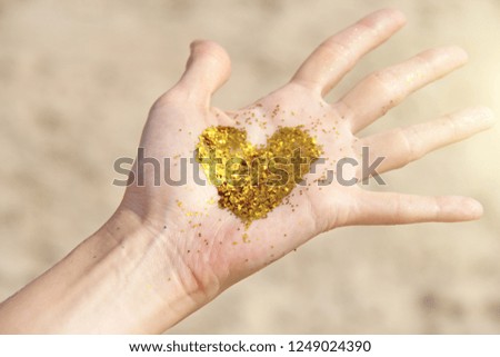 A golden shining heart lies in the hands of the girl. Golden heart. Design with copy space. Top view.