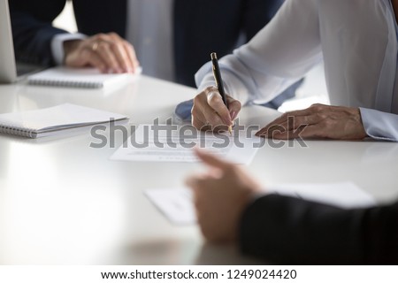 Businesspeople gathered together at business meeting after successful negotiations ready to sign agreement official paper close up focus on businesswoman hands holds pen affirm contract with signature Royalty-Free Stock Photo #1249024420