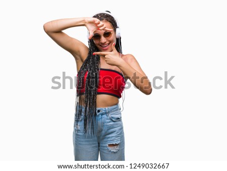 Young braided hair african american with birth mark wearing headphones over isolated background smiling making frame with hands and fingers with happy face. Creativity and photography concept.