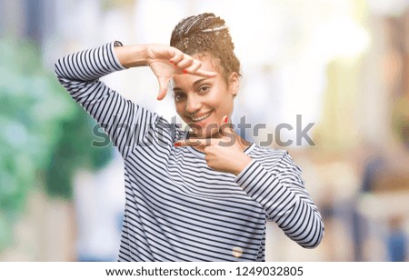 Young braided hair african american girl wearing sweater over isolated background smiling making frame with hands and fingers with happy face. Creativity and photography concept.