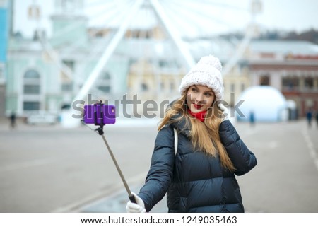 Beautiful blonde woman tourist wearing knitted cap, taking selfie at the street in winter. Space for text