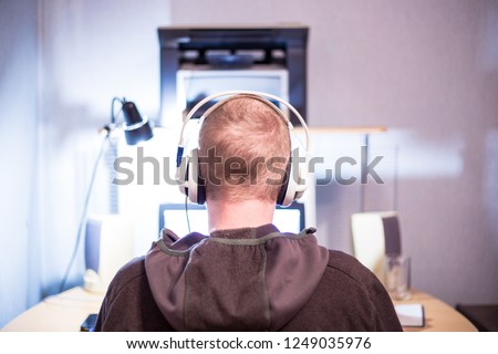 young man sitting in headphones at the computer, the view from the back