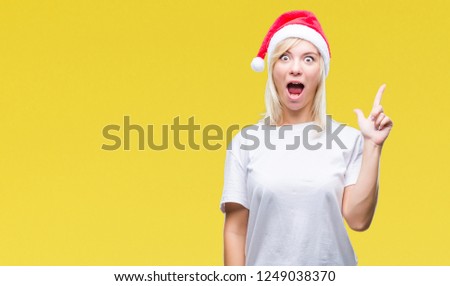 Young beautiful blonde woman wearing christmas hat over isolated background pointing finger up with successful idea. Exited and happy. Number one.